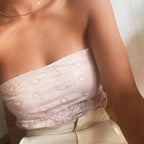 A woman in a light pink, patterned strapless top and beige high-waisted pants wears the elegant LLUME Jewelry Marie Chain necklace, seated indoors near a white wall.