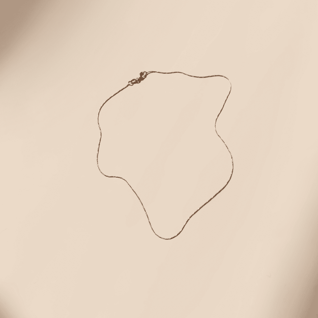 The Golden Hour Chain by LLUME Jewelry is a delicate 18k gold filled necklace with a thin chain and small clasp, displayed in a wavy shape on a plain light beige background.
