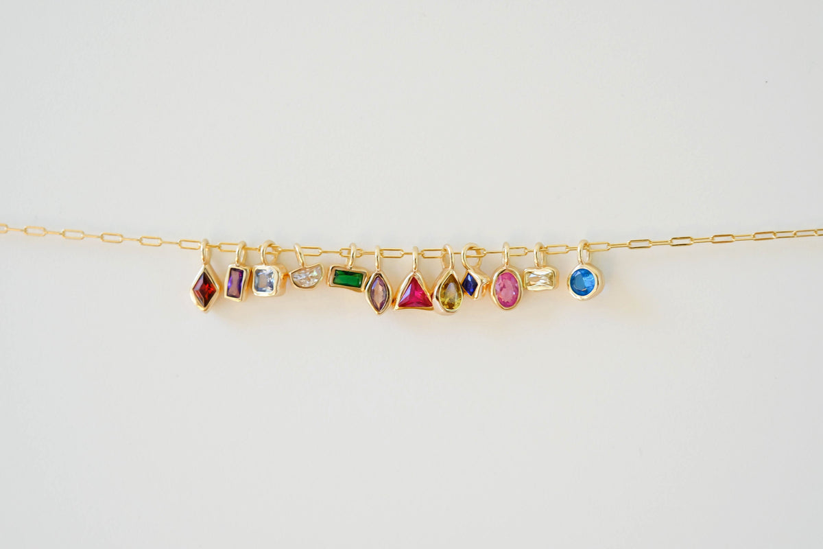 The LLUME Jewelry Build a Birthstone Necklace features a gold chain with colorful, gold-plated charms in oval, round, square, and rectangular gemstone shapes, shown on a white background.