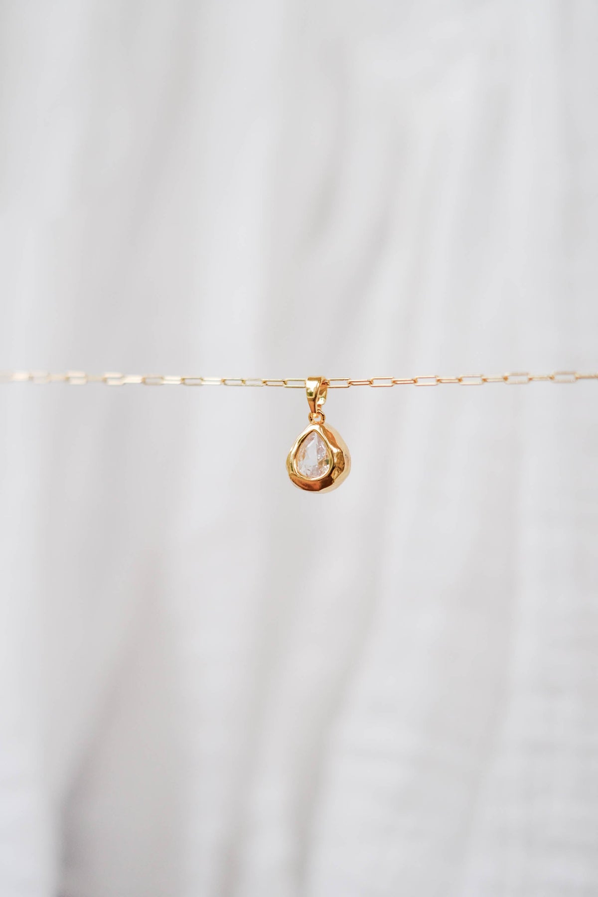 The LLUME Jewelry Build a Charm Necklace features a delicate gold chain with a teardrop clear gemstone pendant and gold-filled charms, beautifully displayed on a soft white background.
