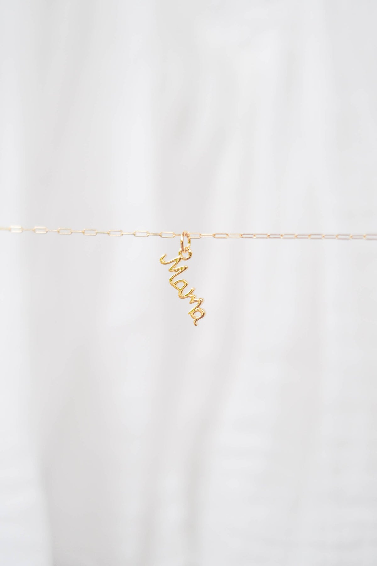 The LLUME Jewelry Build a Charm Necklace features a delicate gold chain with a cursive "mama" pendant and gold-filled charms, displayed on a soft white background—ideal for personalizing or creating your unique charm necklace.