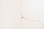 The LLUME Jewelry Cross Necklace showcases a dainty gold-plated chain with a cross pendant, elegantly displayed against a simple light background.