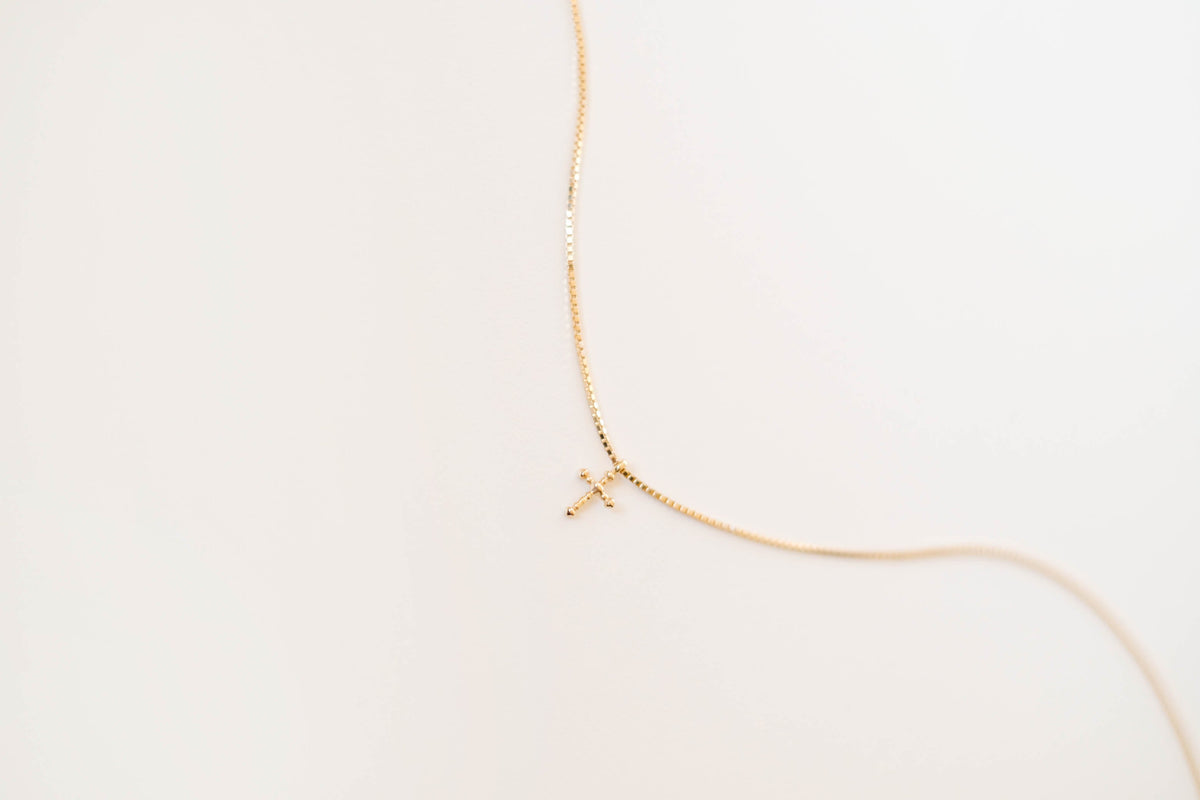 The LLUME Jewelry Cross Necklace showcases a dainty gold-plated chain with a cross pendant, elegantly displayed against a simple light background.