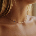 Woman wearing the Celeste gold chain choker dotted with tiny multicolored enamel beads at the throat
