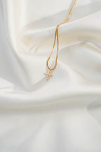 The LLUME Jewelry Cross Necklace, featuring a gold plated chain, is beautifully displayed on soft white silky fabric.
