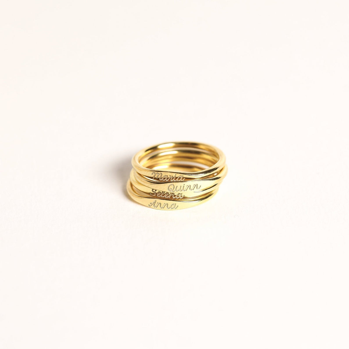 Four stacked Ann Skinny Name Rings in Rose Gold, engraved with Maria, Quinn, Greta, and Anna, shine on a plain white background—making a thoughtful Christmas gift for her.