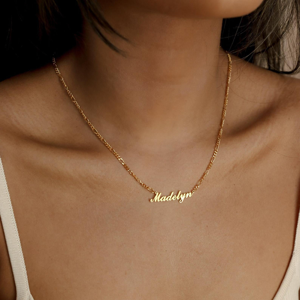 A woman wears a minimal style Carrie Name Necklace in Figaro Chain with the name Madelyn in elegant cursive letters.