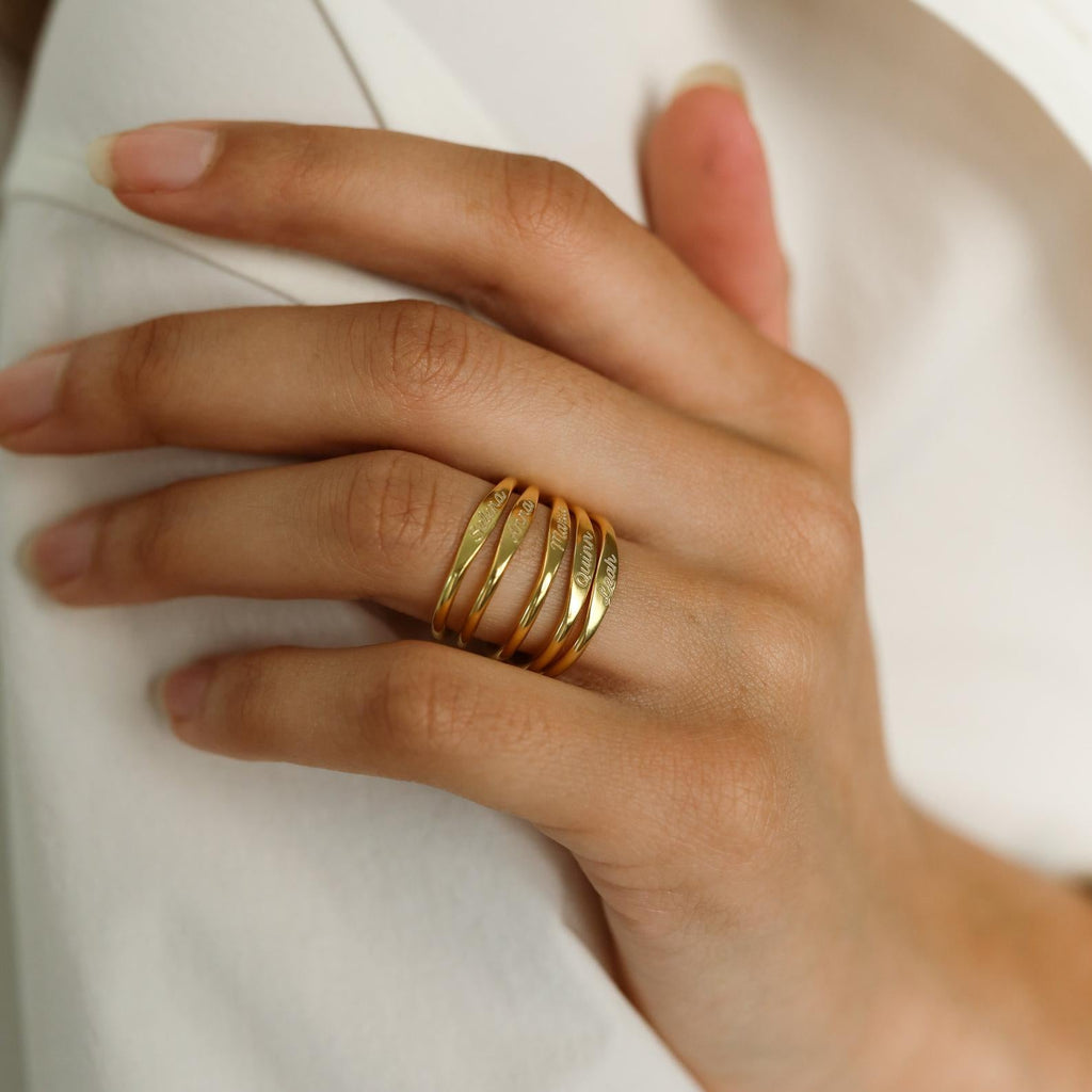 A hand with natural nails showcases the Ann Skinny Name Ring in Rose Gold, part of a stacking ring set, resting on white fabric—an elegant Christmas gift for her.