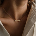 A minimal style gold Carrie Name Necklace in Figaro Chain featuring the name Madelyn, worn by someone in a cream-colored shirt.