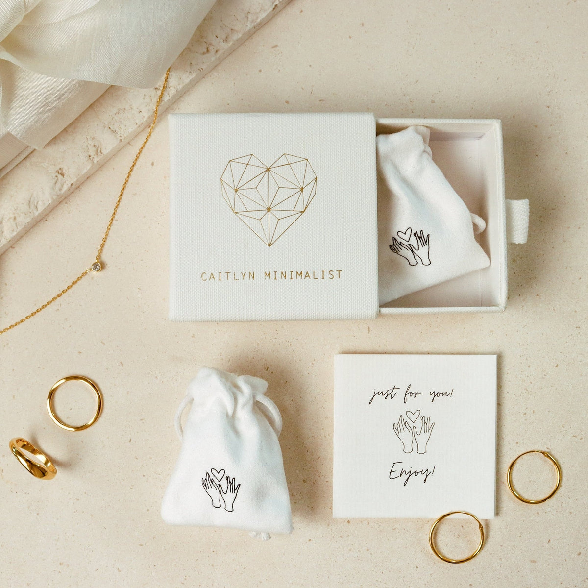 Mellow Name Heart Necklace displayed on a beige surface, featuring a dainty chain and packaged in a box labeled Caitlyn Minimalist.