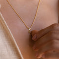 A close-up of a woman's chest wearing a delicate gold chain necklace with a polished gold letter 'J' pendant. The pendant rests at the center of her chest.