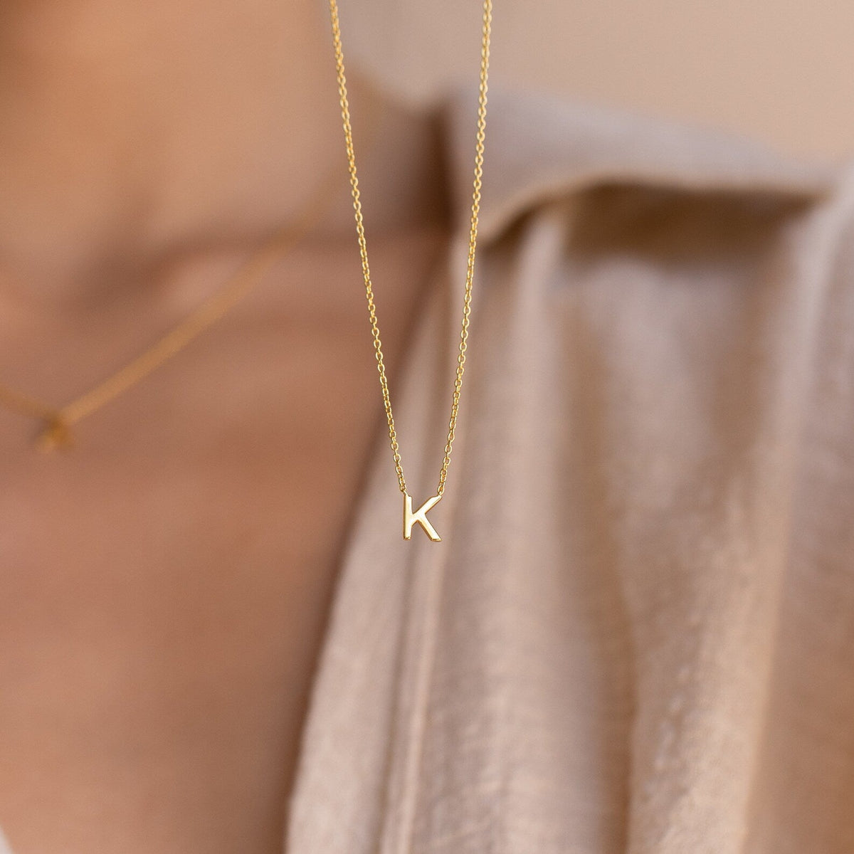 Dainty Initial Necklace featuring a gold letter K pendant, styled over a beige shirt with a blurred background—an ideal customizable accessory and thoughtful Christmas gift.