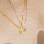 Two Mini Initial Tag Necklaces—a gold one with an "R" and a silver one with a "W"—rest on a textured surface. These personalized necklaces make a thoughtful Christmas gift and are perfect for adding custom style.