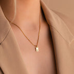 The Mini Initial Tag Necklace, featuring your chosen letter pendant and shown styled over a beige blazer, makes a thoughtful personalized Christmas gift.