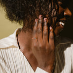 A smiling person touches their cheek, wearing the Duo Baguette Birthstone Ring with personalized gemstones, paired with a light blouse.