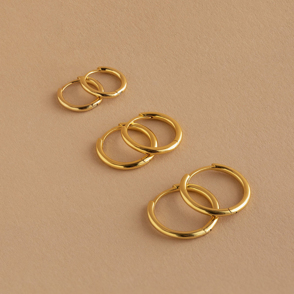 The Mini Bold Hoops Set—three pairs of classic hoops in small, medium, and large—are arranged on a beige surface.