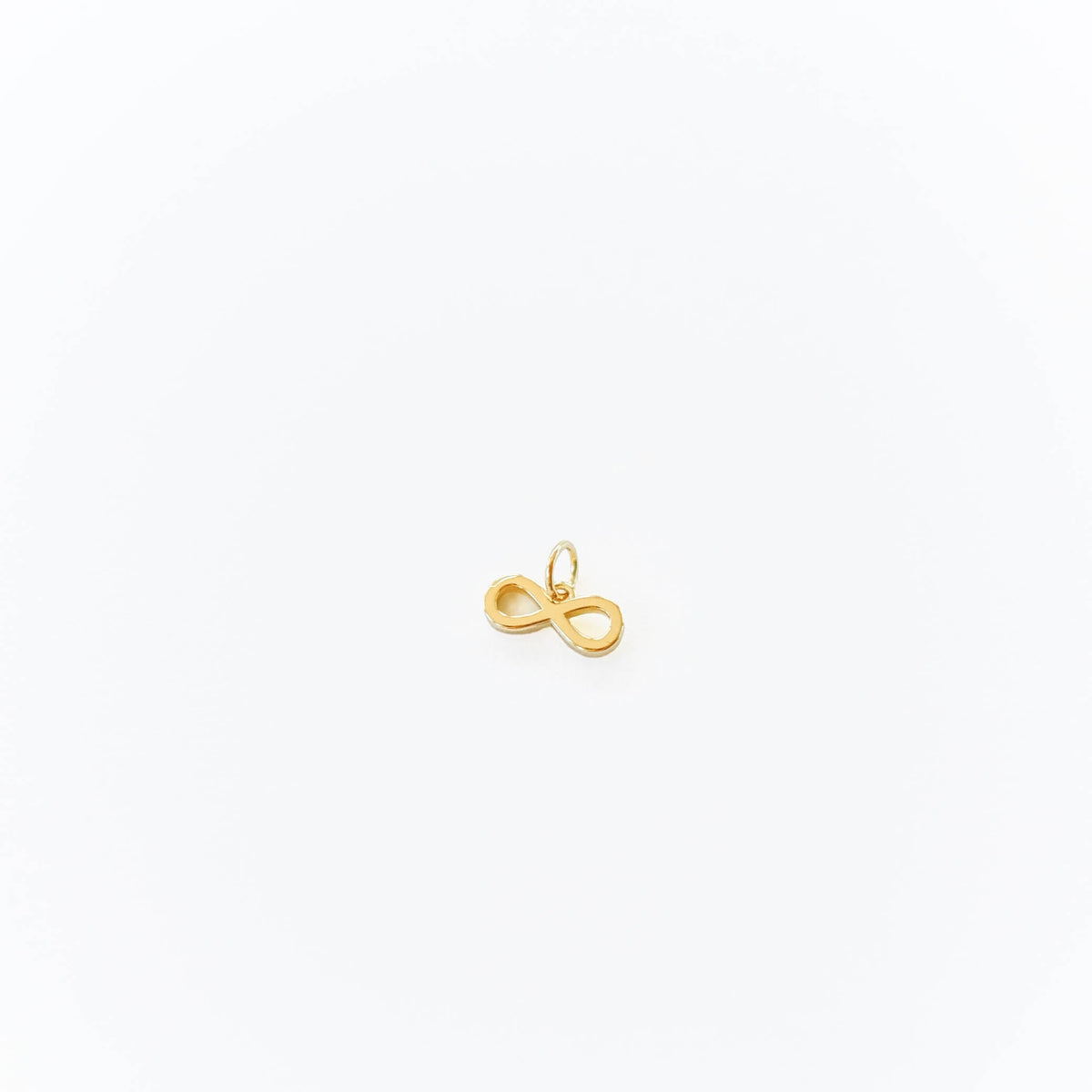A small gold infinity pendant by LLUME Jewelry, designed with a loop for adding to the Build a Charm Necklace, is shown on a plain white background.