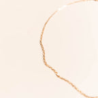The Harlow Chain by LLUME Jewelry, an 18k gold filled necklace, is shown against a soft beige background, with its elegant link chain gently curving and slightly out of focus in the image.