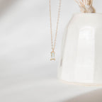 The Daylight Necklace by LLUME Jewelry, featuring a delicate gold-plated chain and a small rectangular clear gemstone pendant, is displayed in front of a white ceramic vase against a soft, minimal background.