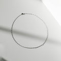 The Colette Necklace Silver by LLUME Jewelry, crafted from sterling silver, is arranged in an oval on a smooth, light surface with soft shadows—a versatile and elegant accessory.
